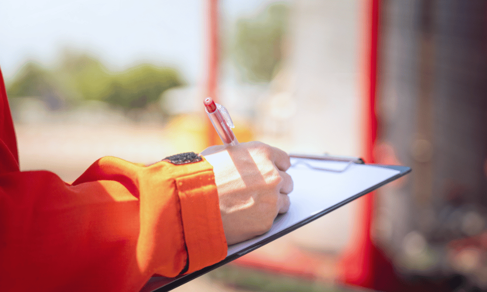 worker in safety gear writes on clipboard